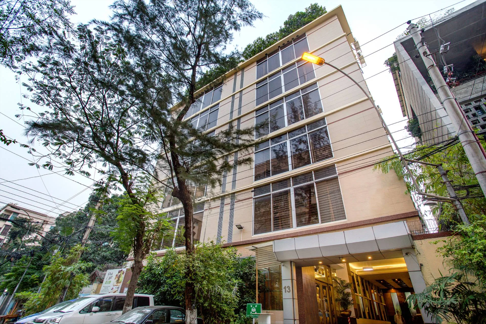 Street view of the Ascott The Residence Dhaka building, with glass panels and trees in front