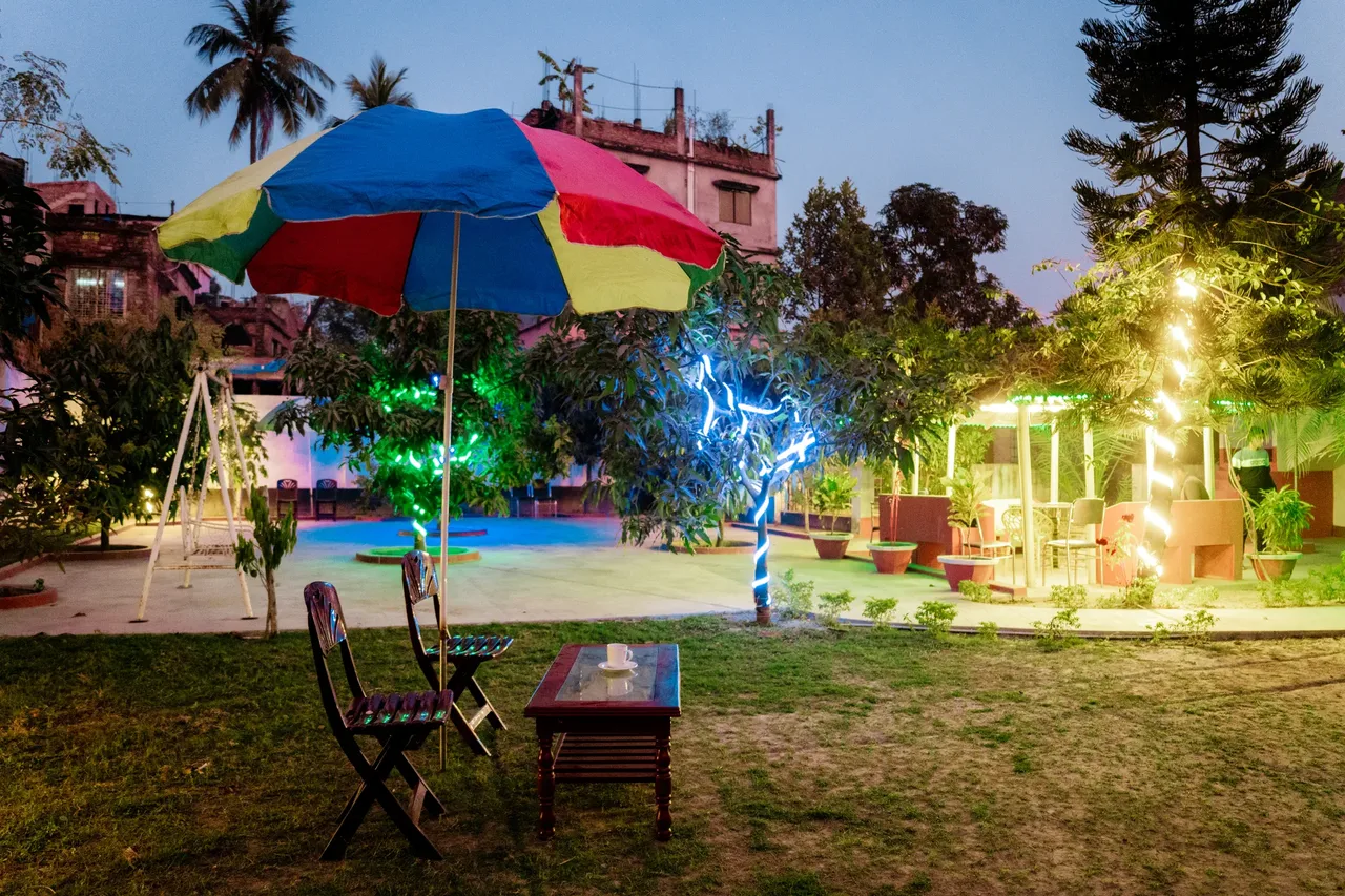 Lawn with a parasol, chairs and play area lit at dusk