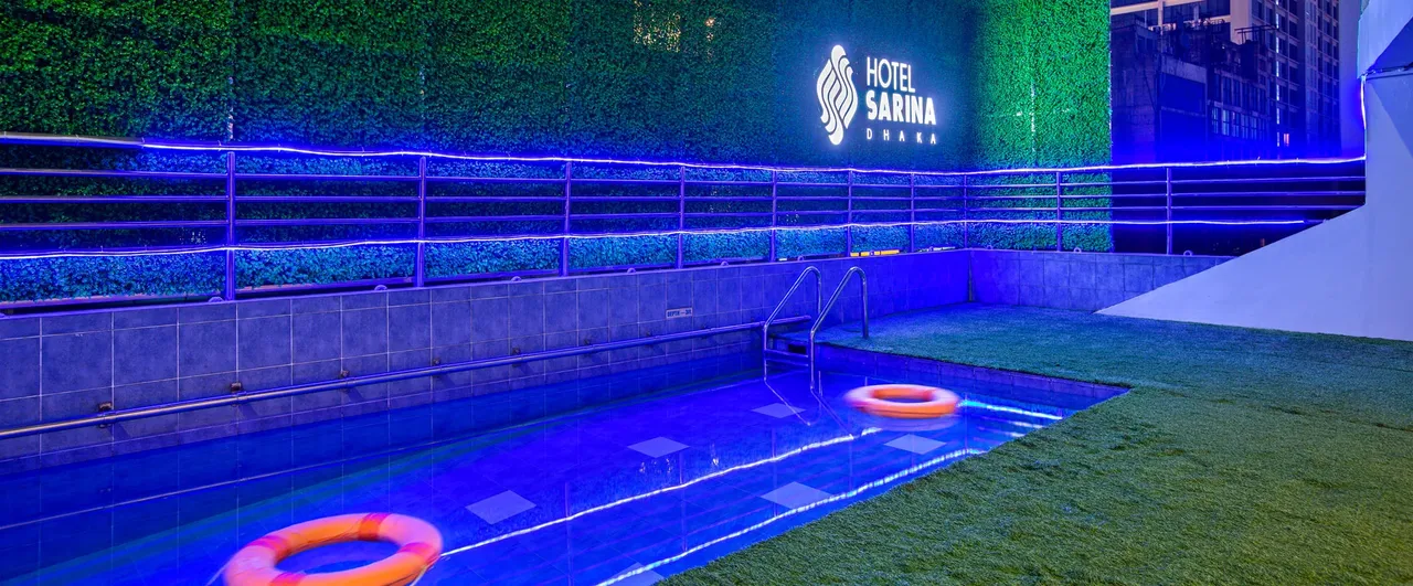 Outdoor pool at Hotel Sarina lit up at night, with the hotel sign behind