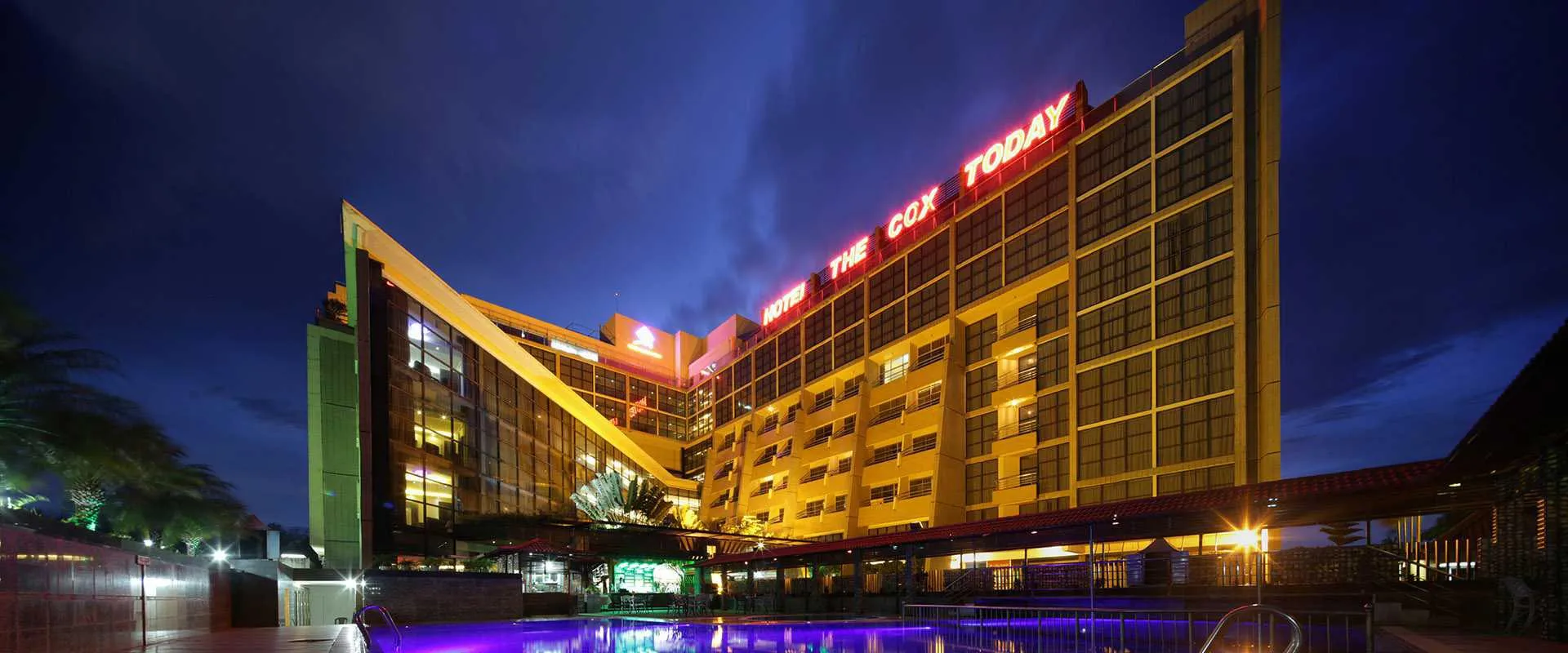 Hotel The Cox Today building lit up at dusk beside the pool